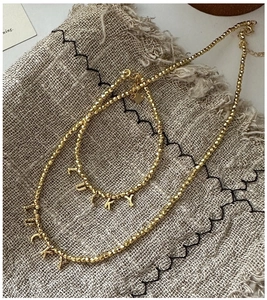 Macro detail of gold beaded jewelry set featuring LUCKY pendants on a rustic linen texture