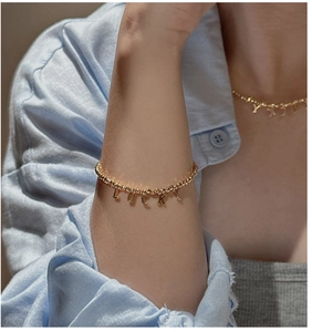 Detailed view of gold beaded bracelet with LUCKY letter pendants on model's wrist
