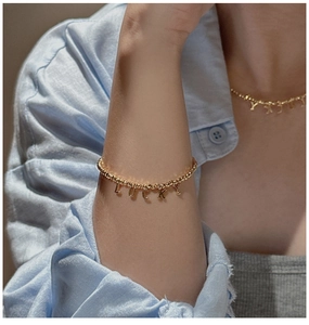 Detail of gold beaded bracelet and necklace set with LUCKY charms on linen fabric