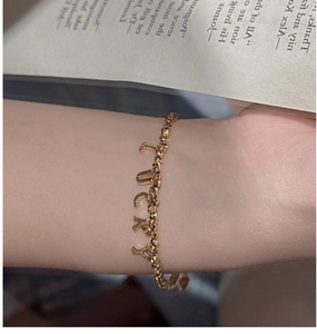 Close-up of a gold beaded bracelet with a Lucky letter pendant worn on a wrist