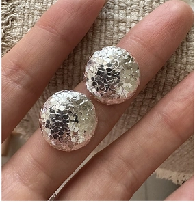 Macro shot of silver stud earrings with hammered fish scale texture on textured linen background