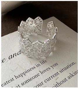 Detailed view of silver open ring with intricate geometric lace hollow design on text paper