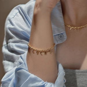 Gold beaded necklace and bracelet set with LUCKY pendant on a model in denim shirt