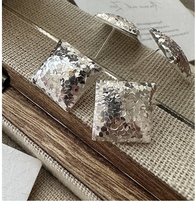 Macro detail of S925 sterling silver square stud earrings with hammered scale texture