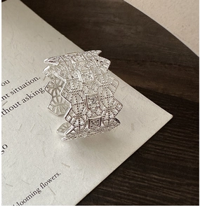 Macro detail of silver lace hollow ring featuring clear cubic zirconia on texture paper