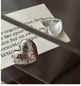 Macro detail of silver heart stud earrings with textured surface and smooth backing
