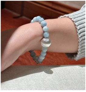 Détail d'un bracelet en aigue-marine avec grosse perle argentée gravée sur une manche