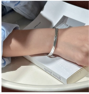 Detailed close-up of silver honeycomb textured open bangle bracelet on a book