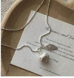 Detail of S925 silver necklace with brushed ball pendant and rhinestone leaf on paper