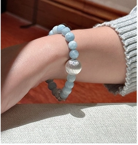 Détail macro du bracelet en perles d'aigue-marine avec breloque cœur au poignet d'une femme