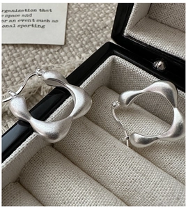Close-up of matte silver irregular square earrings on a beige velvet jewelry box tray