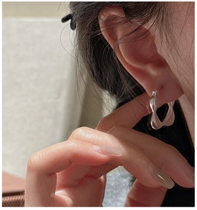 Macro view of wave twisted S925 sterling silver hoop earrings worn on ear