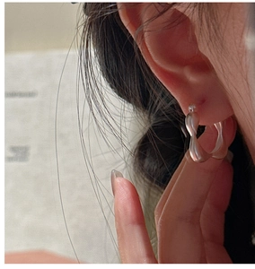Close-up of minimalist matte silver twisted wave hoop earring worn on model ear