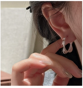 Close-up of matte square silver earrings with twisted lava texture worn by a model