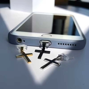 Three cross-shaped phone charms in gold, silver, and black on a smartphone
