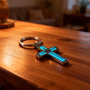 Luminous stainless steel cross keychain with blue glow on a rustic dark wood surface