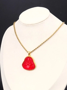Close-up of a red laughing Buddha pendant on a golden rope chain around a neck model