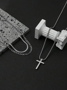 Close-up of layered stainless steel cross necklace and snake chain on decorative stone