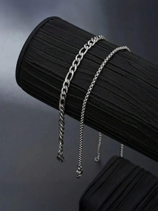Detail of silver stainless steel Figaro and bead chain bracelets on a black jewelry stand