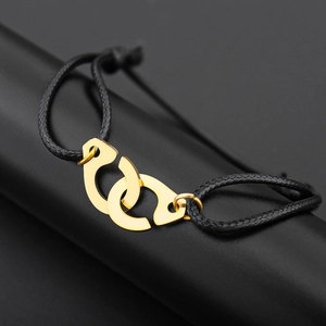 Macro detail of gold-plated interlocking handcuffs on a black braided rope bracelet
