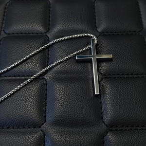Collana con pendente a croce in acciaio inossidabile lucido su sfondo in pelle nera