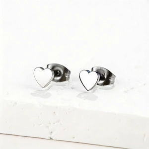 Polished stainless steel minimalist heart stud earrings displayed on white stone