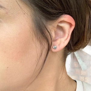Minimalist silver heart stud earring in polished stainless steel shown on ear lobe