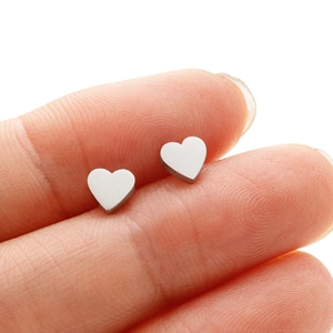 Close-up of small silver heart-shaped stainless steel stud earrings held by hand