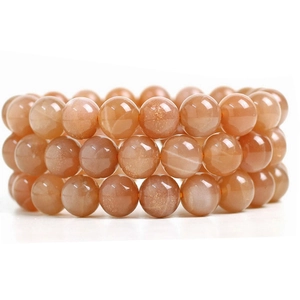 Macro detail of three stacked orange sunstone bead bracelets with golden shimmer and glow