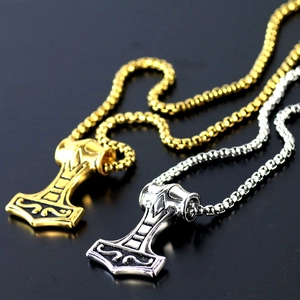 Vintage Mjölnir hammer pendants in gold and silver steel on a black reflective surface