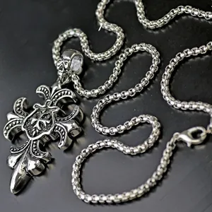 Macro shot of gothic fleur-de-lis cross pendant in vintage silver on a box chain