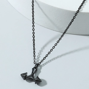 Détail macro du pendentif haltère tenu par une main en noir mat sur un support en pierre