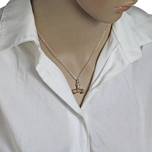 Detailed view of a gold dumbbell pendant necklace worn by a model on a white shirt