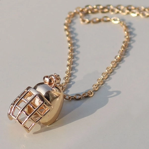 Close-up of a golden tactical helmet pendant with fine metal texture on a thin chain