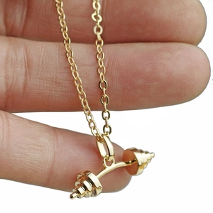 Detailed close-up of a miniature golden dumbbell pendant held in hand for size comparison