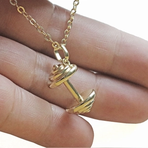 Collier à pendentif haltère doré avec chaîne croisée élégante présenté sur la main pour sport
