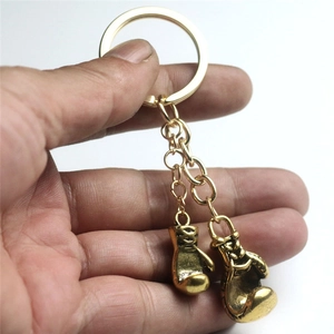 Porte-clés gants de boxe dorés vintage avec deux pendentifs tenu à la main sur fond neutre
