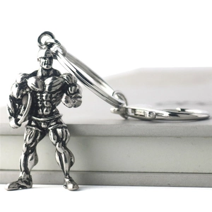 Detail view of a vintage silver muscular man keychain resting on a grey book edge