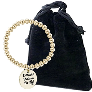 Detail of gold beaded bracelet with engraved Breathe Believe Be pendant and velvet pouch