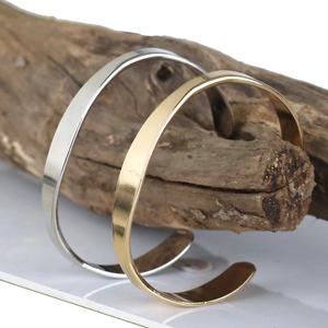 Detailed view of minimalist open cuff bracelets in gold and silver on wood