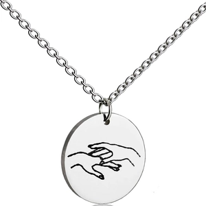 Macro detail of minimalist stainless steel round pendant with hand gesture art engraving