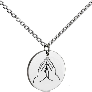Macro shot of silver stainless steel round pendant with prayer hands engraved detail