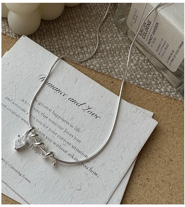 Detail of silver snake chain necklace featuring a heart zircon pendant on beige background