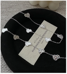 Silver long necklace featuring heart-shaped pendants with textured glitter finish on black tray