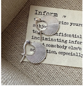 Detailed view of silver pleated fan-shaped earrings on rustic beige linen background