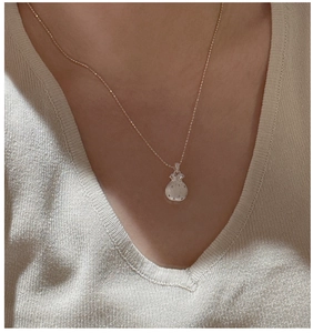 Macro detail of a S925 silver lucky bag pendant necklace worn on a beige knit sweater