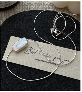 Detailed macro of silver snake chain with rectangular Baroque pearl pendant on velvet