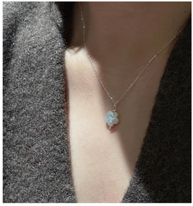 Vue détaillée du collier en argent S925 avec perle baroque et fleur sur un pull gris