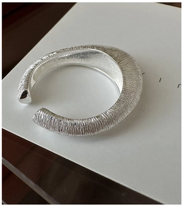 Makroaufnahme minimalistischer silberner offener Ring mit gebürsteter Metallstruktur und Design