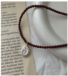 Close-up of red agate beaded necklace with silver ammonite shell pendant on vintage page